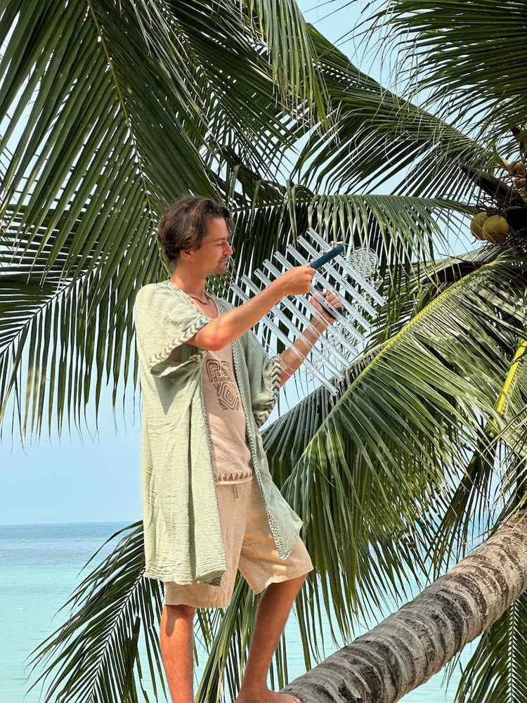 
                    
                      Sever in linen holding Crystal Harp Chakra C framed by palm fronds with blue sea and sky
                    
                  